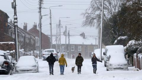 People and a dog walk through thick snow blanketing a residential street in West Kyo, County Durham