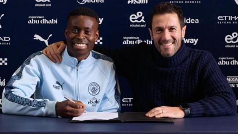 Manchester City defender Marc Guehi (left) smiles as he signs his contract next to director of football Hugo Viana (right)