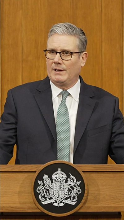 Starmer, who wears glasses, stands at a lectern in No 10